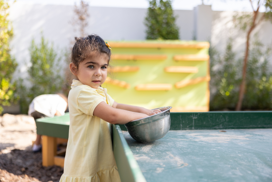 Toddler outdoors with her hands in a steel bowl.