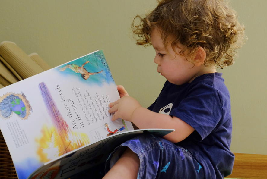 Toddler turning a book page while sitting on the floor.