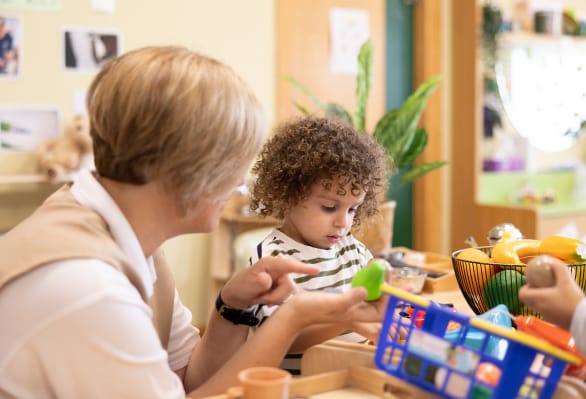 A woman is helping a child at a table in a playroom.