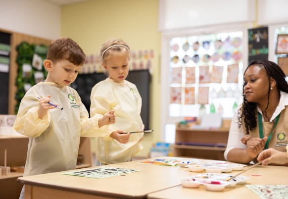 A group of children are painting at a table in a classroom.