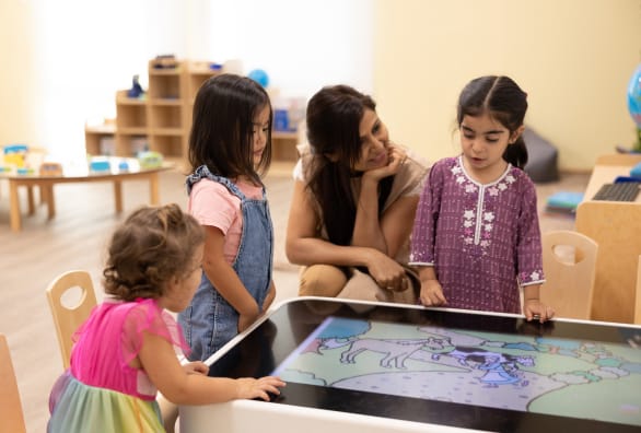 A group of children playing with an interactive table in a classroom.