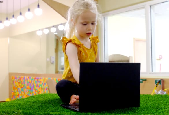 A little girl is using a laptop in a room.