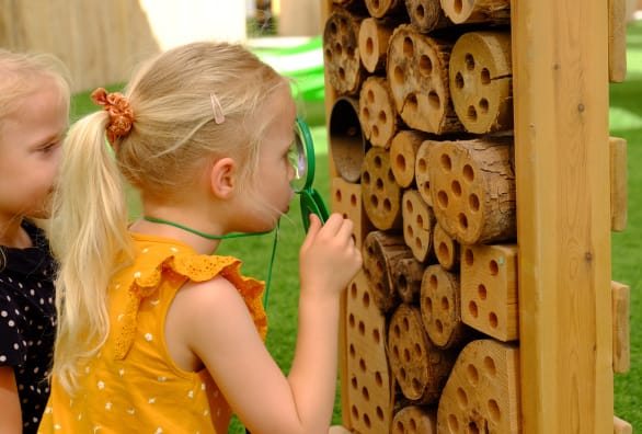 Two little girls looking at a wooden bug house.