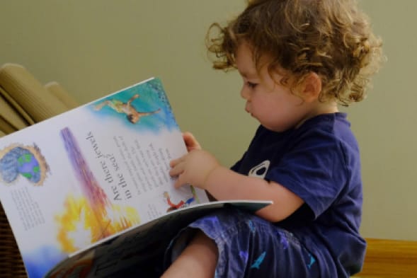 A young boy is sitting on a stool reading a book.