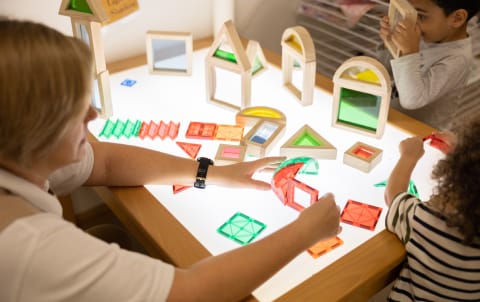A woman and a child playing with toys at a table.