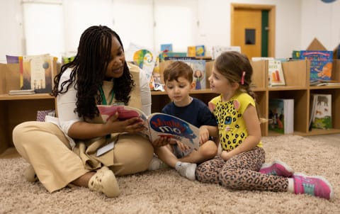 A teacher reads a book to a group of children in a classroom.