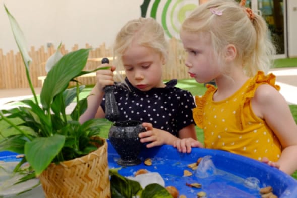 Two little girls playing with plants in a pond.