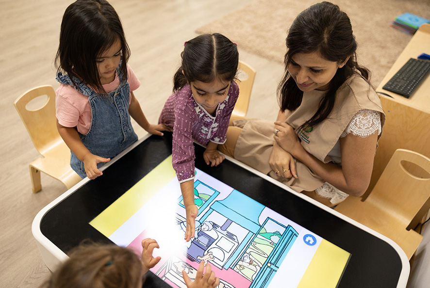 A group of children playing with an interactive table in a classroom.