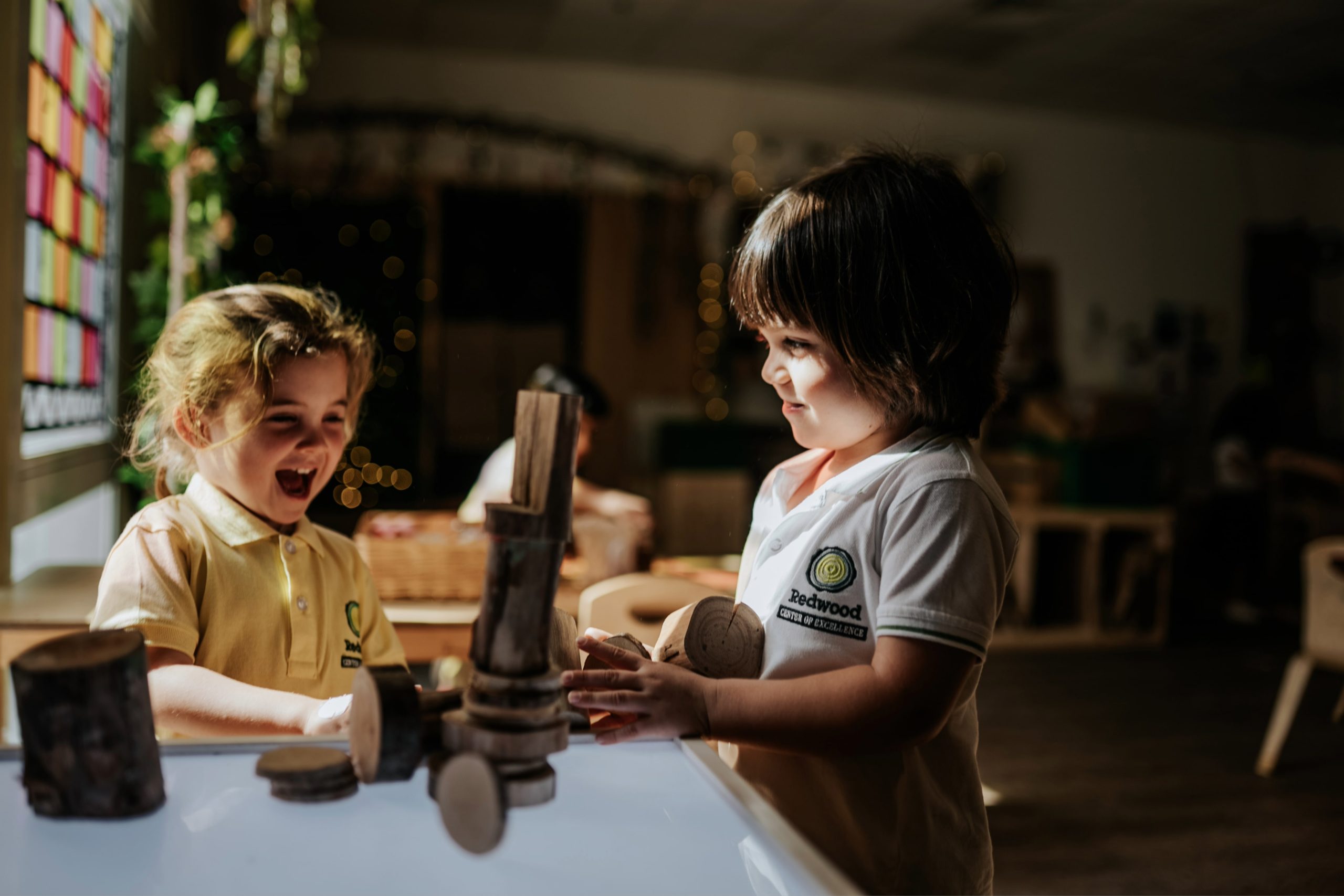 Two children playing with wooden toys in a classroom.